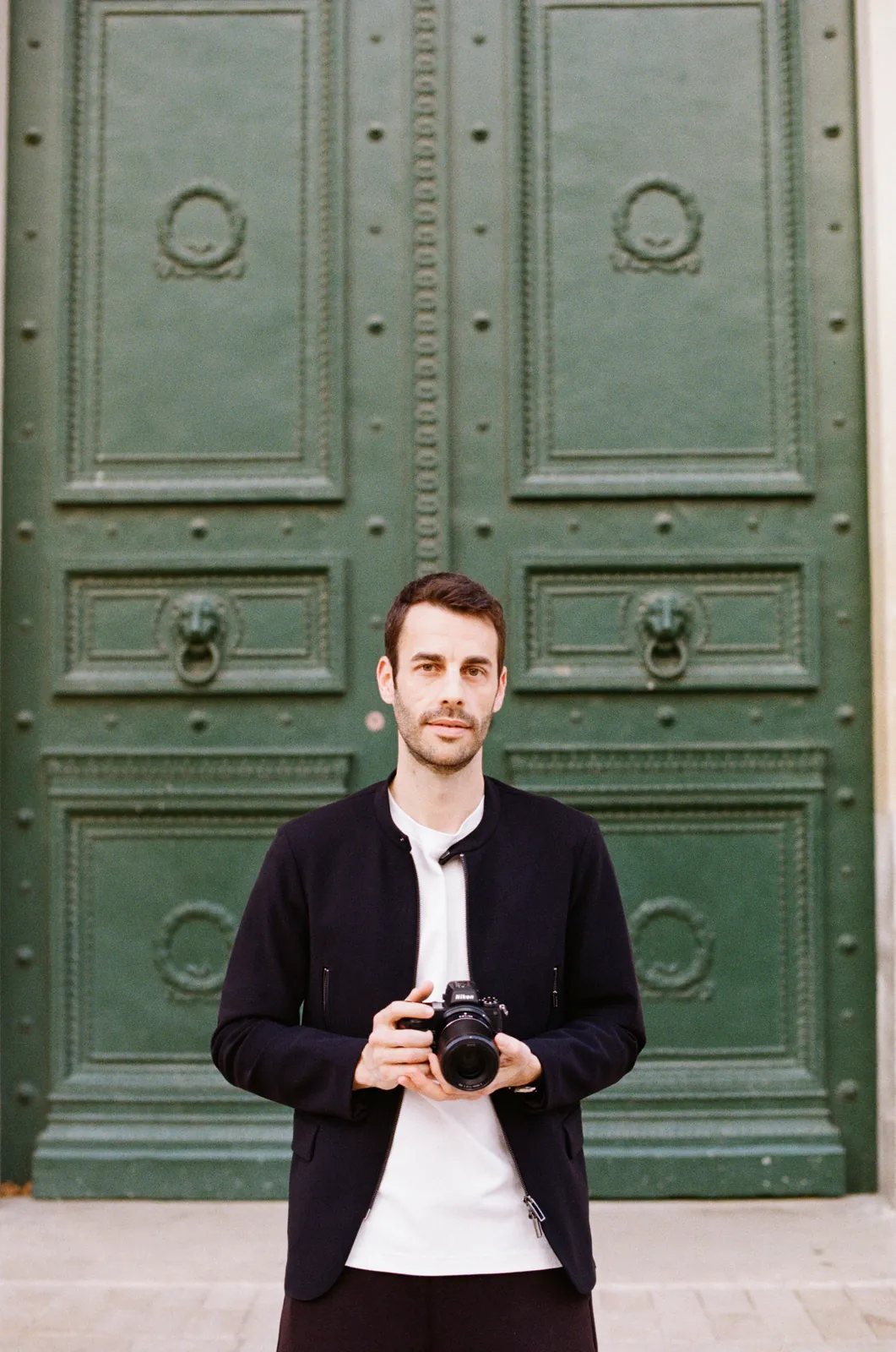 Guillaume Belguedj, appareil à la main, devant une porte cochère à Aix-en-Provence