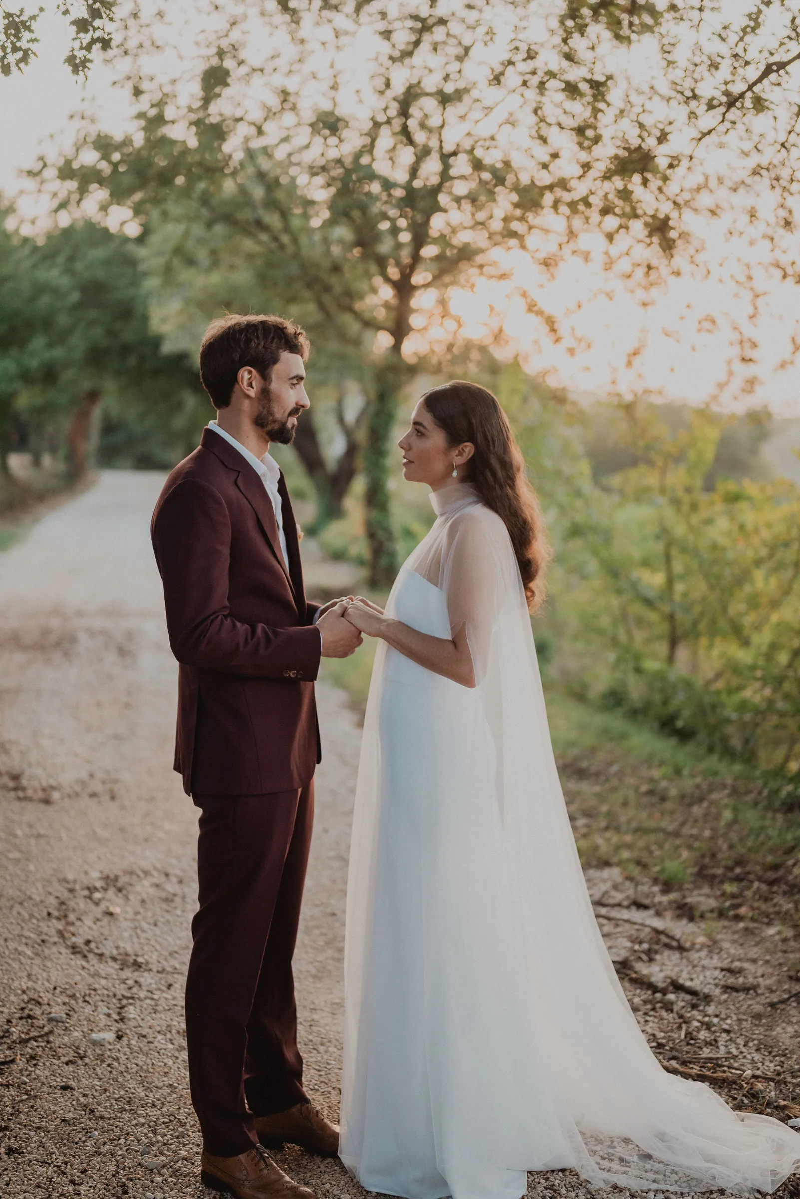 Les mariés se tiennent la main sur le chemin, au coucher du soleil